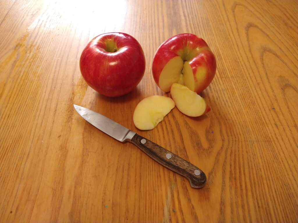 Two Honeycrisp apples, one has sections cut from it. Knife lies on the table.