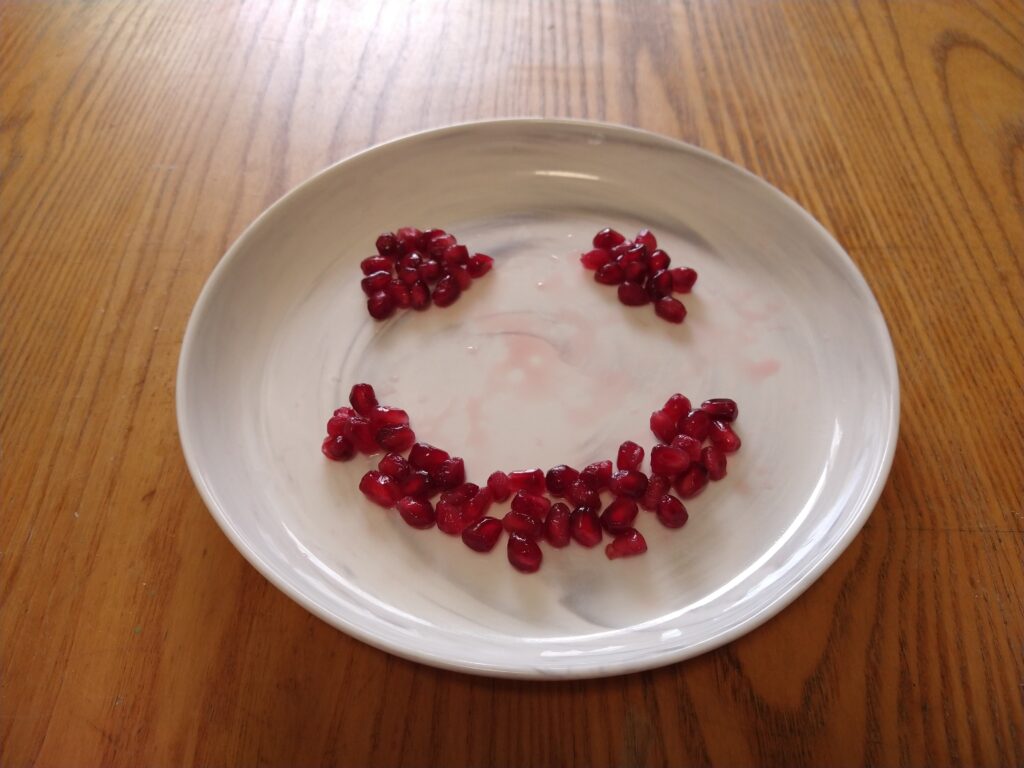 Pomegranate arils arranged into the shape of a smiley on a plate. 