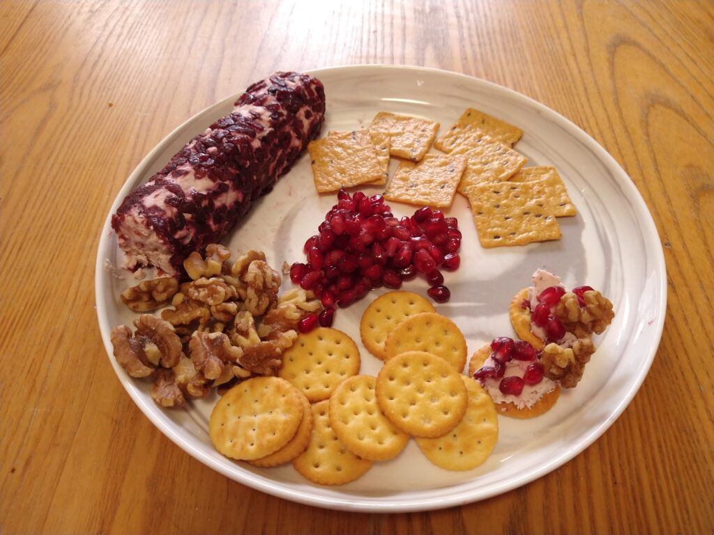 Plate with a fruity cheese spread, pomegranate arils, crackers, and walnuts.