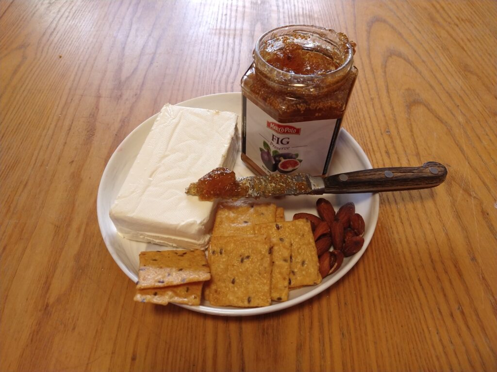Plate with jar of preserved figs, crackers, almonds, and cream cheese.